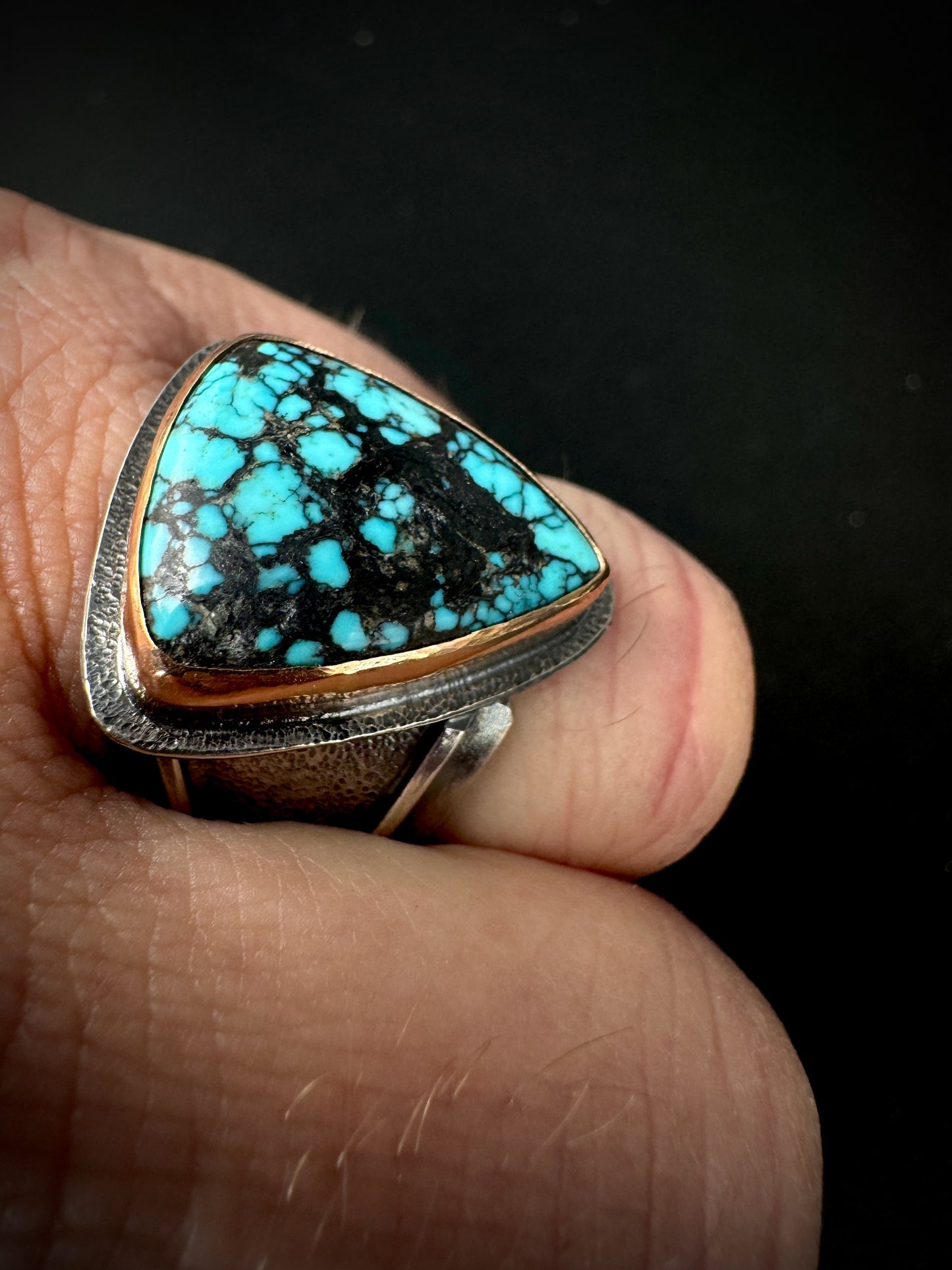 Turquoise stone ring on a finger with a dark background